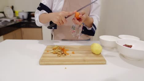 skilled woman chef peeling skin of carrot using sharp knife in kitchen