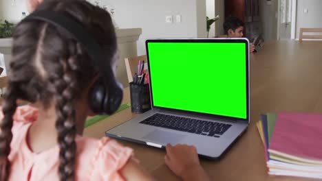 Composition-of-biracial-schoolgirl-on-laptop-online-learning-with-green-screen