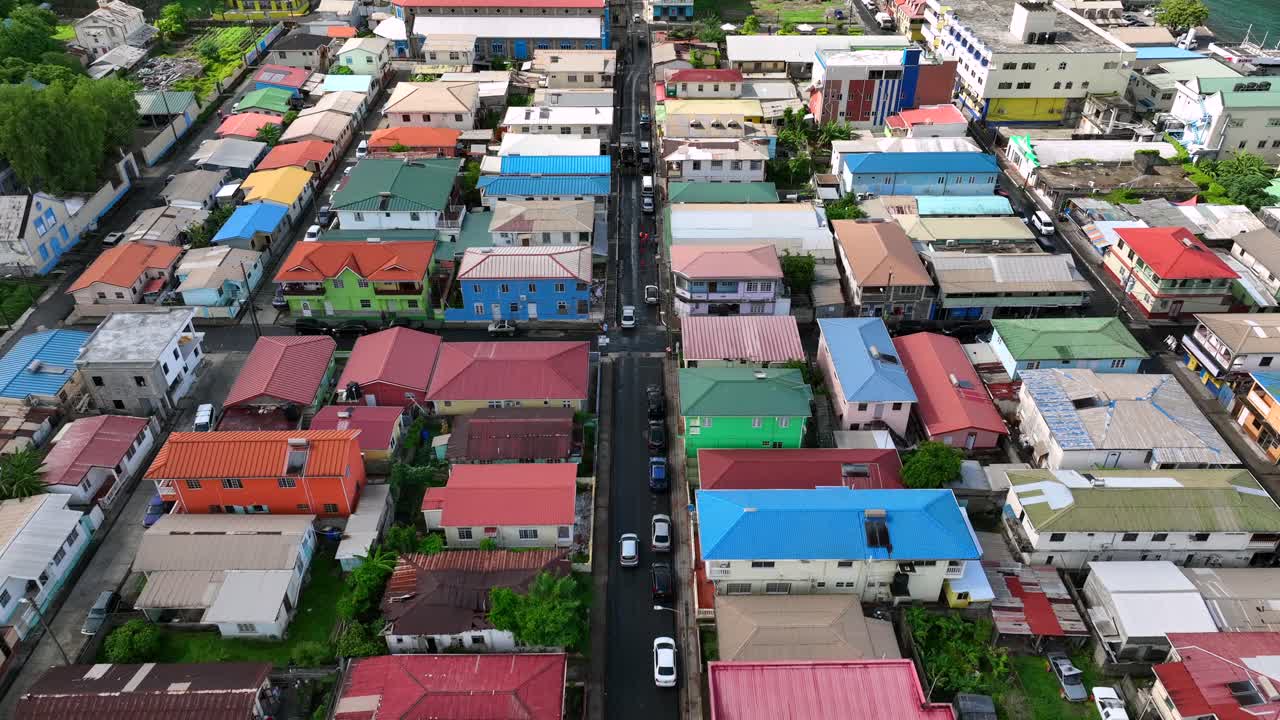 Colorful residential neighborhood rooftops and narrow street with parked cars. Overhead view of a vibrant, densely-packed community in a tropical region. Aerial.
