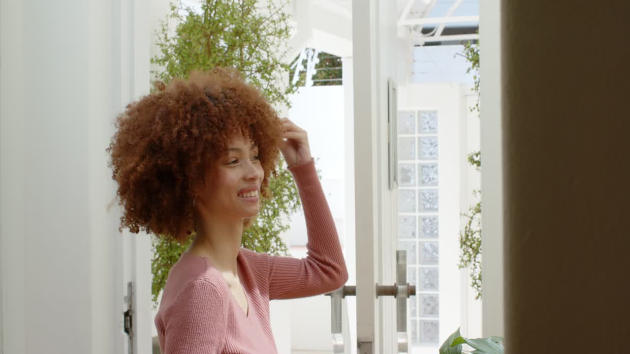 Notando lo specchio, una donna afroamericana si tocca i capelli per acconciare i ricci nel corridoio di casa, spazio per il testo