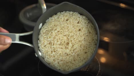 covered pot of boiling water on n electric stove to cook raw whole grain rice in a medium saucepan