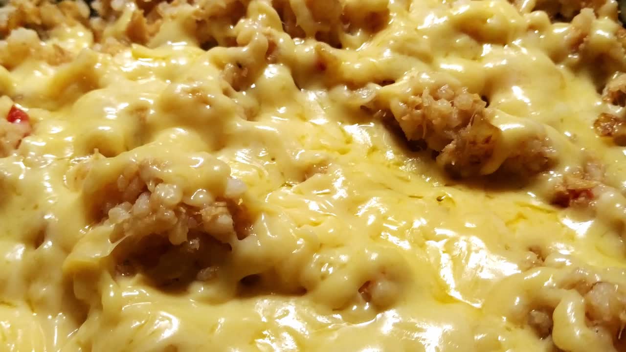 cerca de queso rallado que se ha derretido sobre una sartén llena de arroz salteado con atún y pimientos rojos, burbujeante y chisporroteante con calor