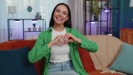young woman makes symbol of love, showing heart sign to camera, express romantic positive feelings