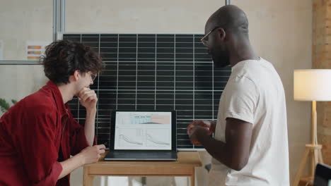 multiethnic colleagues discussing project on laptop by solar panel in office