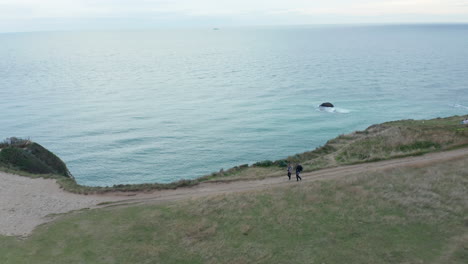 Small-Church-on-Hill,-Aerial-forward-tilting-down-revealing-Cliffs-and-Ocean-with-Overcast-Sky