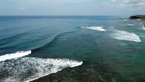 drone shot of waves breaking in tropical place with surfers in the crystal clear water