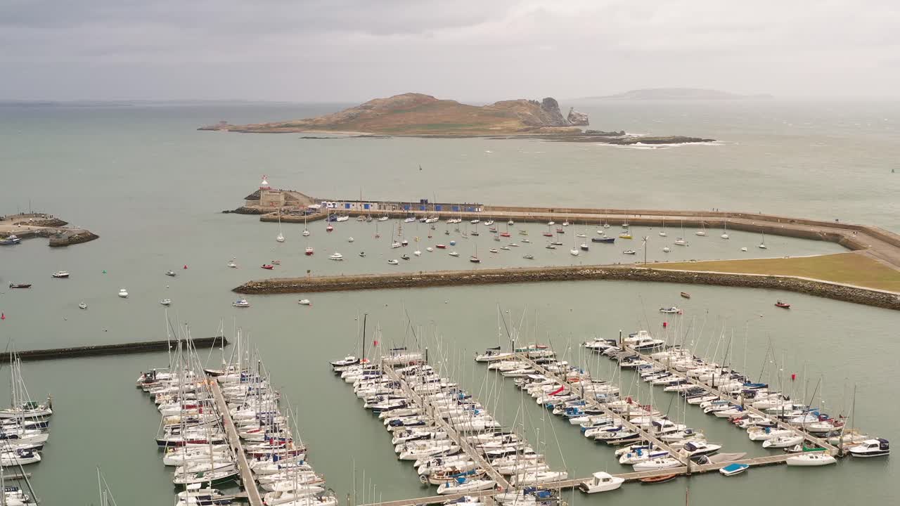 Drone rises above Howth Harbour with boats docked and Ireland's Eye in backdrop