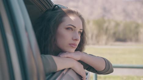 mujer joven tranquila con ojos azules se inclina hacia fuera de la ventana del coche