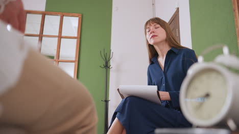 Relational expert seated in calm therapy space with pen and paper in hand, listening attentively to client during reflective session focused on understanding emotions and communication patterns