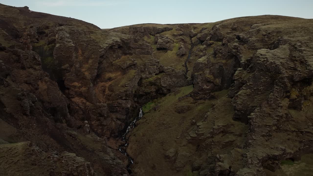 A rugged canyon in northern Iceland features steep volcanic cliffs and a hidden waterfall, showcasing the remote and dramatic landscape.
