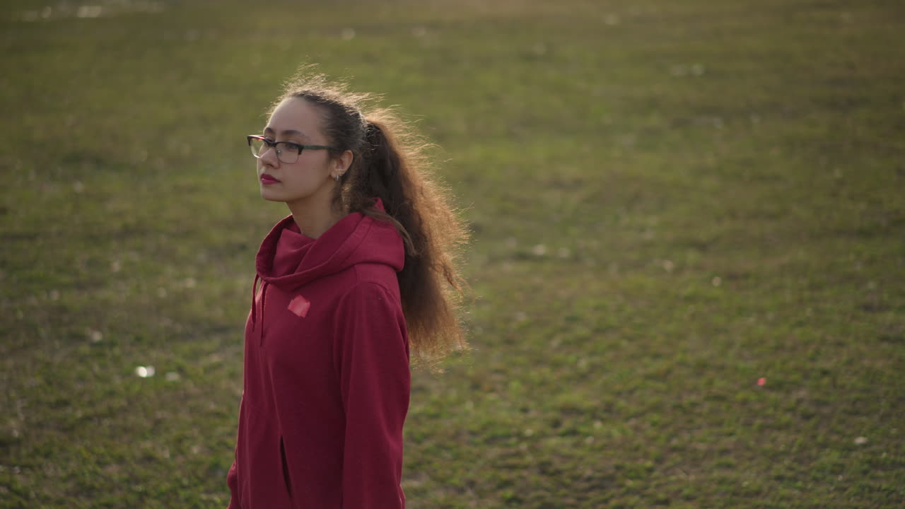Backpacker bevæger sig over mark, silhuet af kvinde i rolig bevægelse, fredfyldt scene af kvinde, der bærer ejendele udendørs, fredfyldt billede af kvinde med rygsæk, der slentrer gennem åbent græsområde