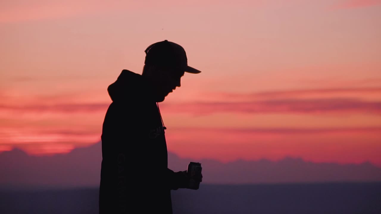 Silhouetted Boy Has Drink on Top of Mountain with Sunset in Backround