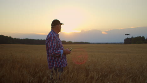 Farmer-holds-remote-controller-with-his-hands-while-quadcopter-is-flying-on-background.-Drone-hovers-behind-the-agronomist-in-wheat-field.-Agricultural-new-technologies-and-innovations.