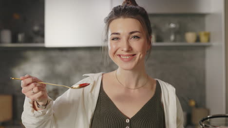 woman tasting food from a spoon while cooking in the kitchen