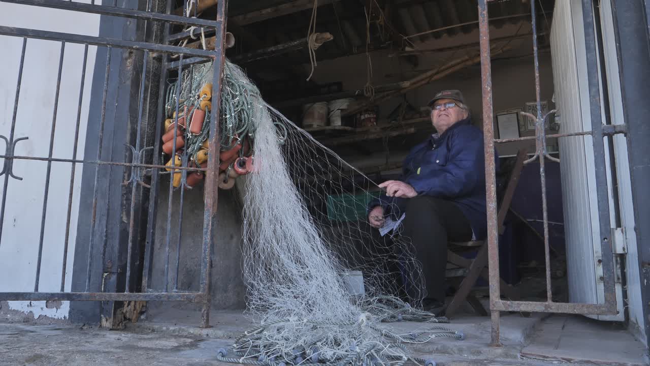 Elderly man talking about his art of mending fishing nets. Static