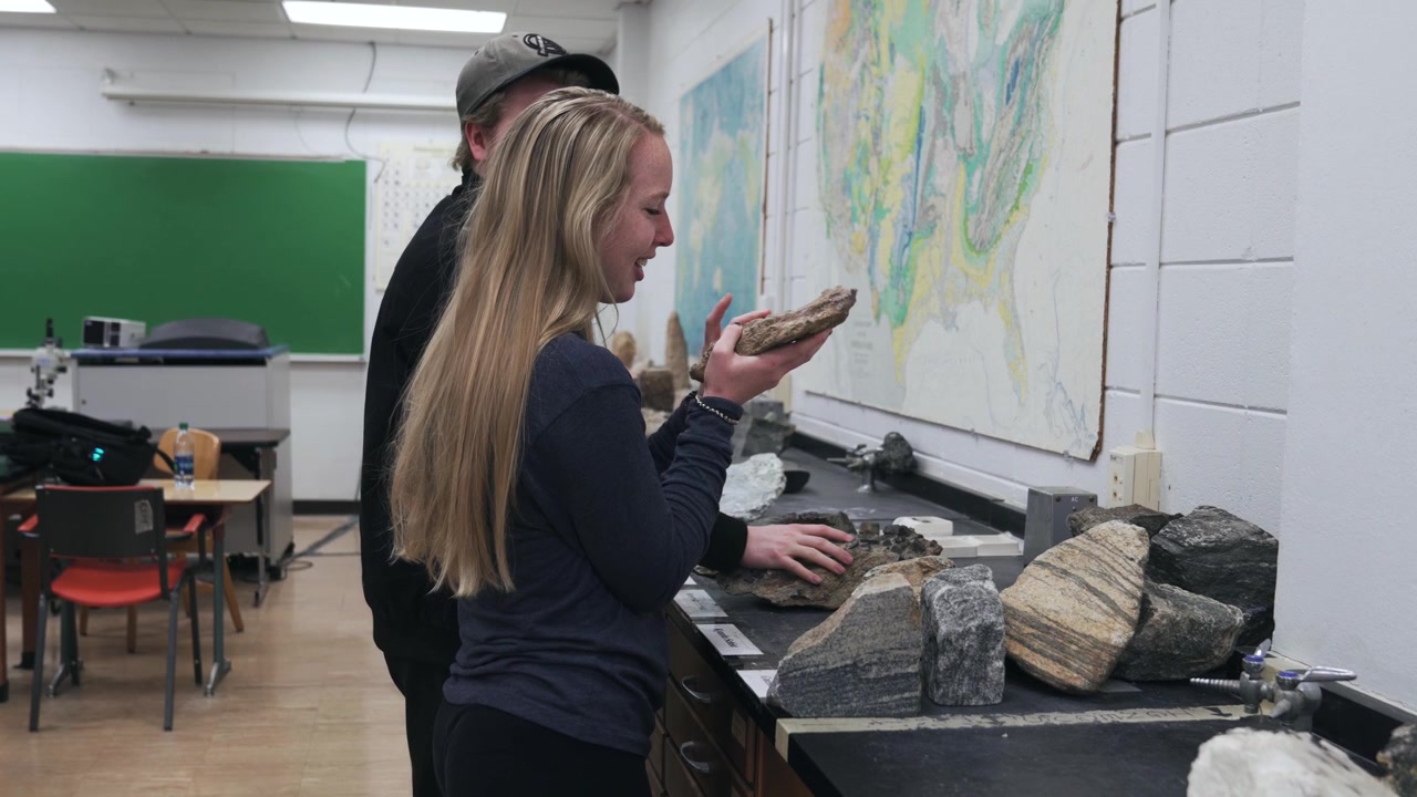 Diversi studenti esaminano e discutono grandi massi per un esame di geologia in un'università.