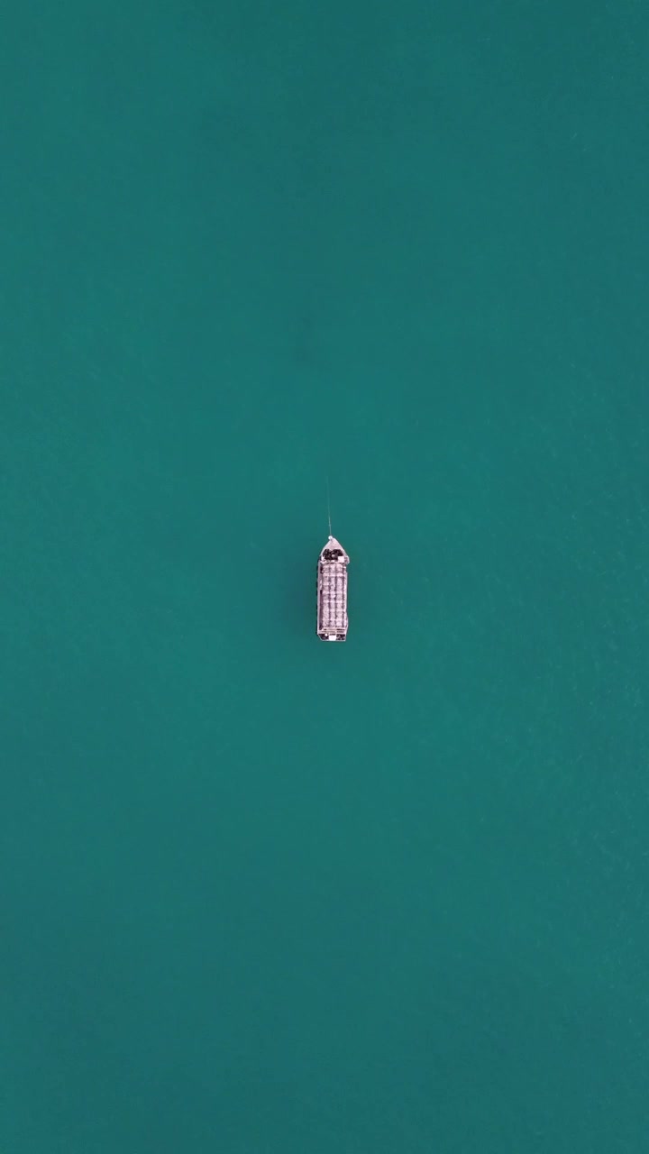 Vista da drone di una barca che galleggia placidamente su acque cristalline turchesi, mostrando la bellezza mozzafiato del paesaggio marino