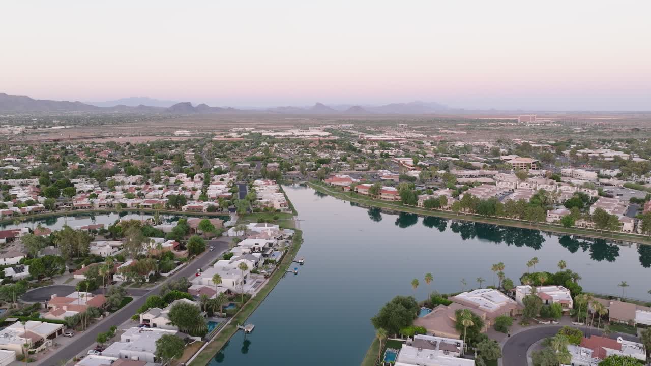 Un sereno lago suburbano circondato da case al tramonto con montagne distanti all'orizzonte, vista aerea.