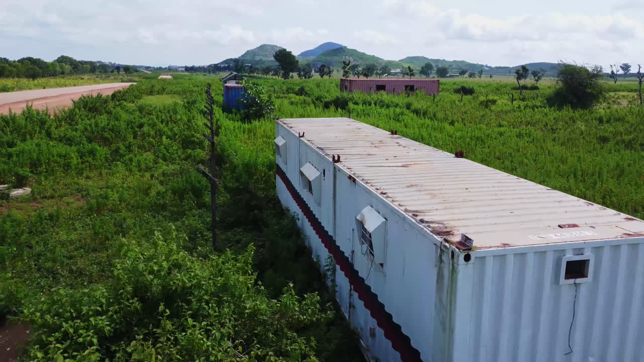 Drone flying over a meadow with long grass and portable cabins standing in the field in rural Nigeria, Africa