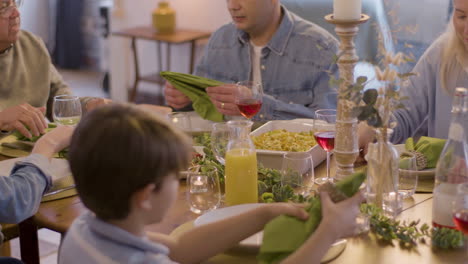 happy family sitting at table in dining room, unfolding napkins and talking before dinner