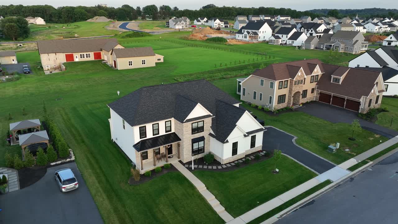 Modern suburban housing development in America. New single-family homes,wide streets, green lawns and early morning light in peaceful neighborhood.Aerial approaching shot. Quiet suburb district in USA