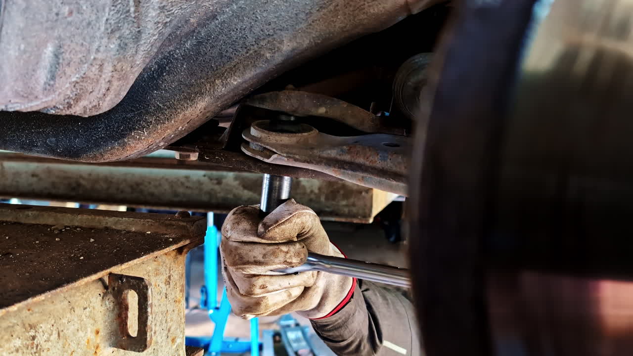Mechanic tightening rear suspension bolt with socket wrench under lifted car during repair