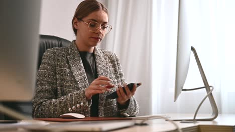 Attractive young woman puts on glasses before working on the computer in the office. Businesswoman in modern office space or coworking open space