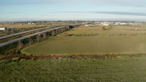 green fields of planted crops line a highway leading to small town in distance