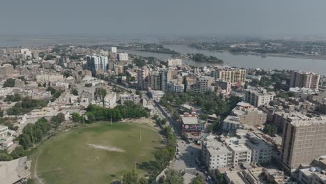 Drohne-Fliegt-über-Die-Stadt-Sukkur-Mit-Hohen-Häusern-Und-Dem-Indus-Fluss-Im-Hintergrund