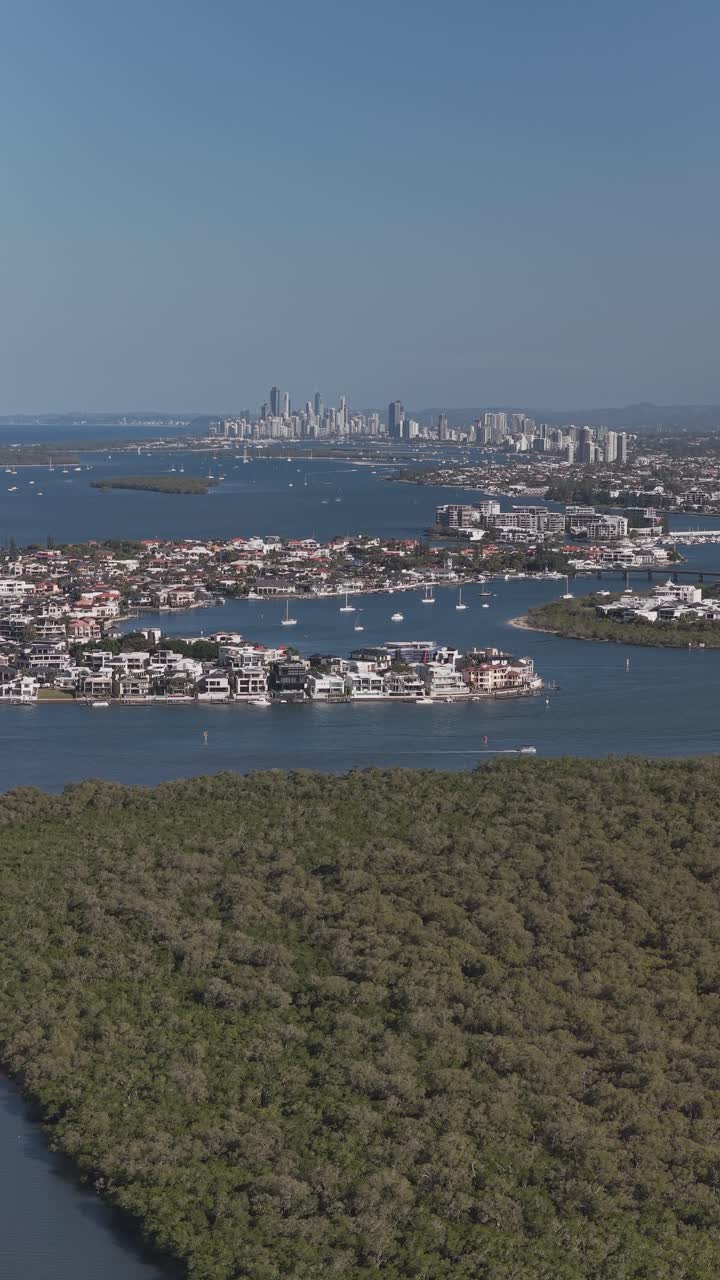 Lussuose case sul lungomare e isole verdi lussureggianti a Paradise Point, Queensland. Skyline della Gold Coast in lontananza. Scatto verticale, aereo.