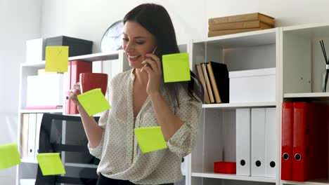 businesswoman in white blouse considering stickers on glass and talking on phone