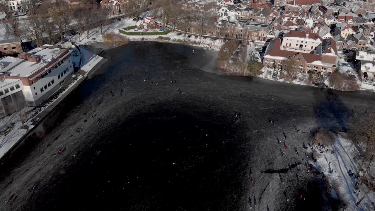 Sideways aerial showing urban winter landscape with people ice skating circling on a large part of a canal in the Dutch city of Zutphen at the edge of the historic town