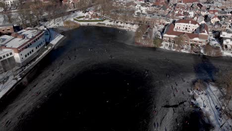 sideways aerial showing urban winter landscape with people ice skating circling on a large part of a canal in the dutch city of zutphen at the edge of the historic town