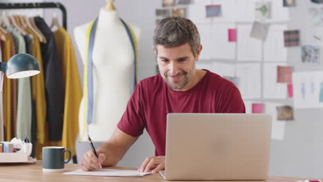 Mature-Male-Fashion-Designer-In-Studio-Working-On-Laptop-Computer