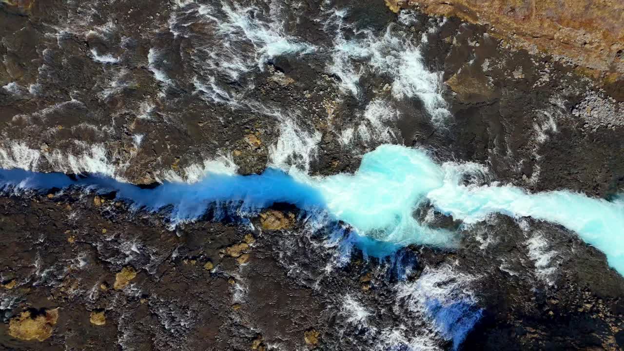 Aerial top down Brúarfoss waterfall in Iceland, featuring vibrant turquoise waters flowing through rugged volcanic terrain