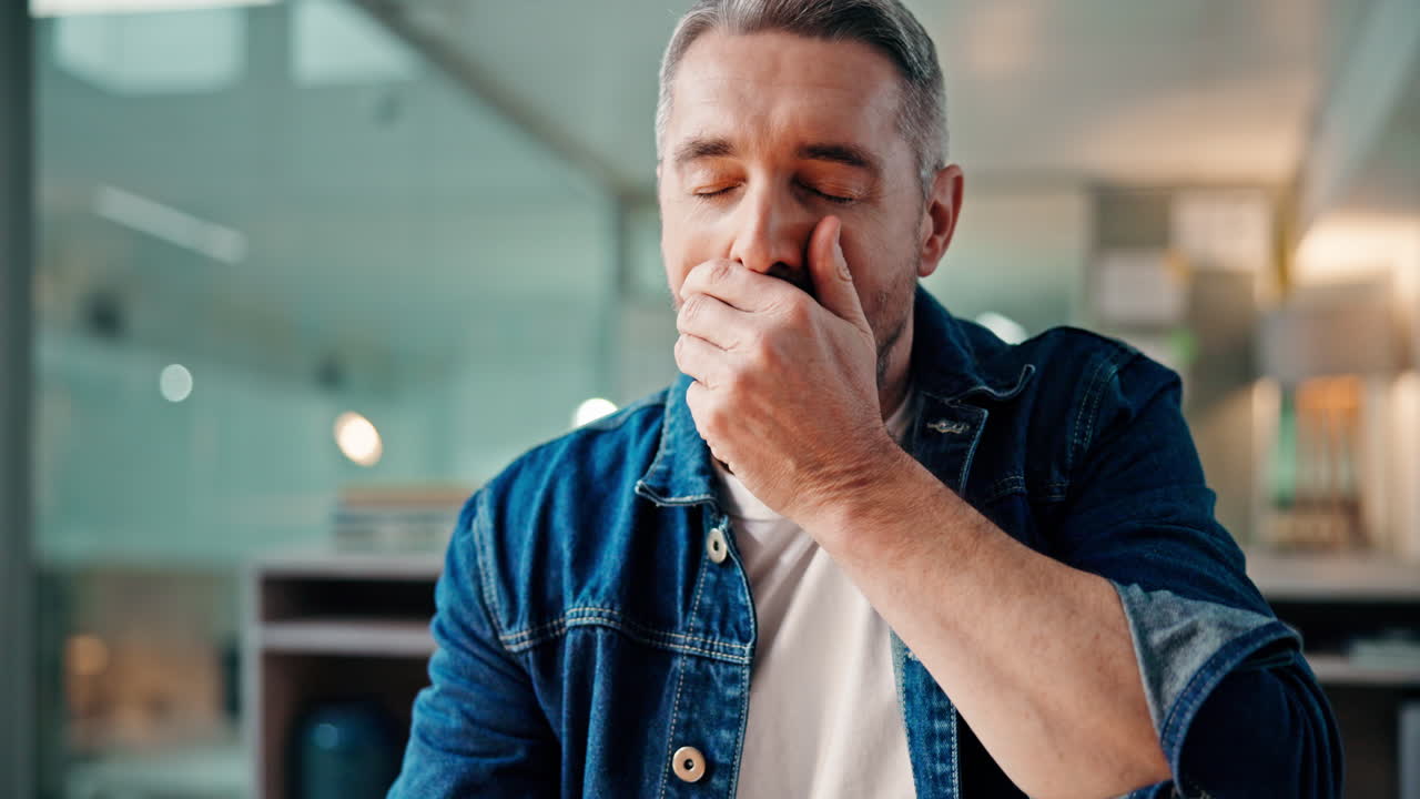 A middle-aged man in a denim shirt looking thoughtful
