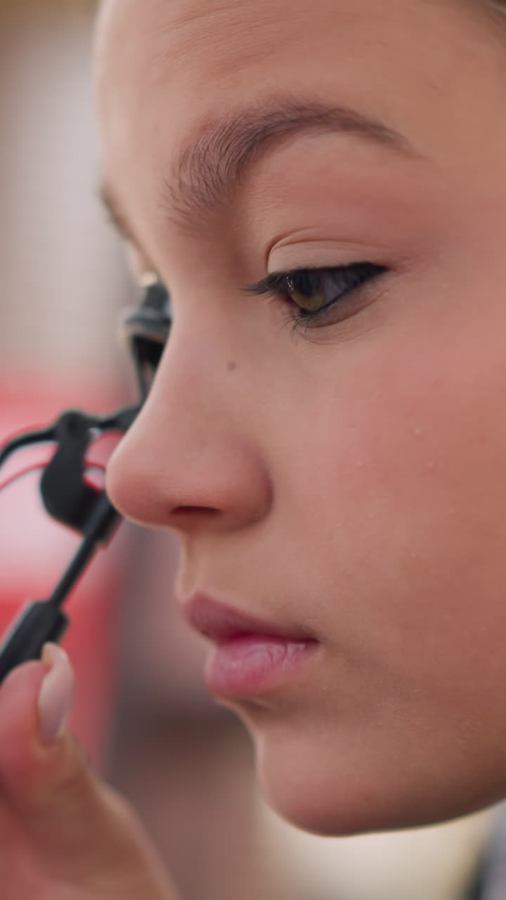 primer plano de perfil de una mujer sin especificar rizando sus pestañas con un rizador de metal, actor preparado posando para la cámara con un ritual tranquilo, luces suaves de estudio y expresión concentrada que resaltan los detalles y el cuidado de la herramienta