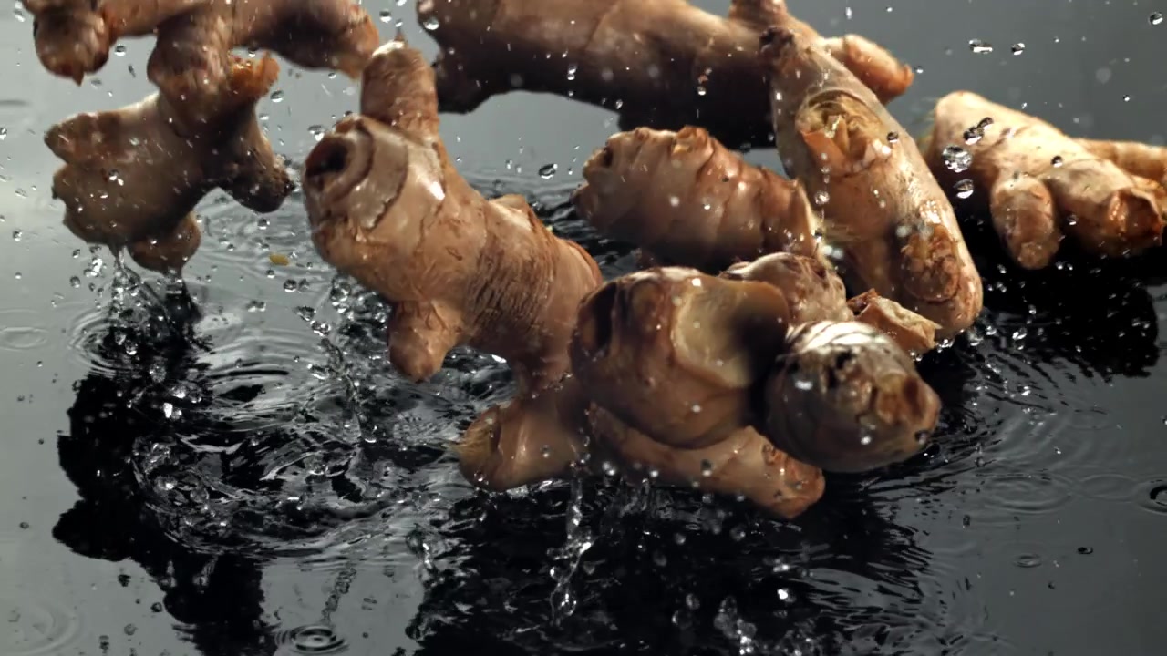 Fresh Ginger Roots Falling into Water with Splashes in Slow Motion