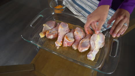 seasoning raw chicken drumsticks with orange spice in glass baking pan