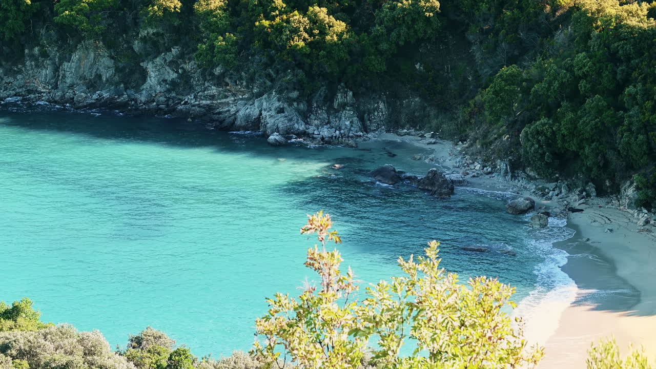 Aegean sea coast with blue transparent water, greenery around, rocks, bushes and trees, view from the drone Greece