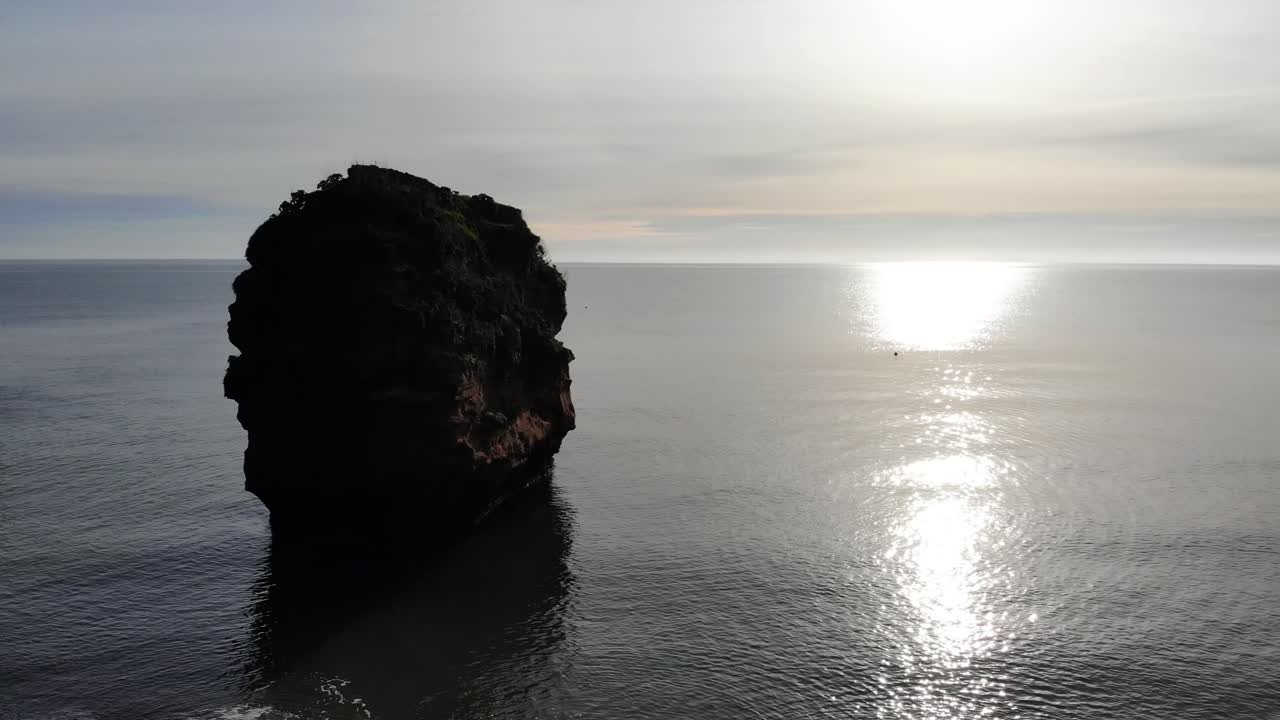 빛에 사암 더미가 있는 잔잔한 바다 위에 일몰의 공중 상승 샷