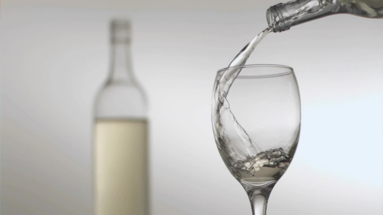 Bottiglia inclinata che si rovescia versando liquido in un calice di vino, coriandoli che fluttuano, scena celebrativa