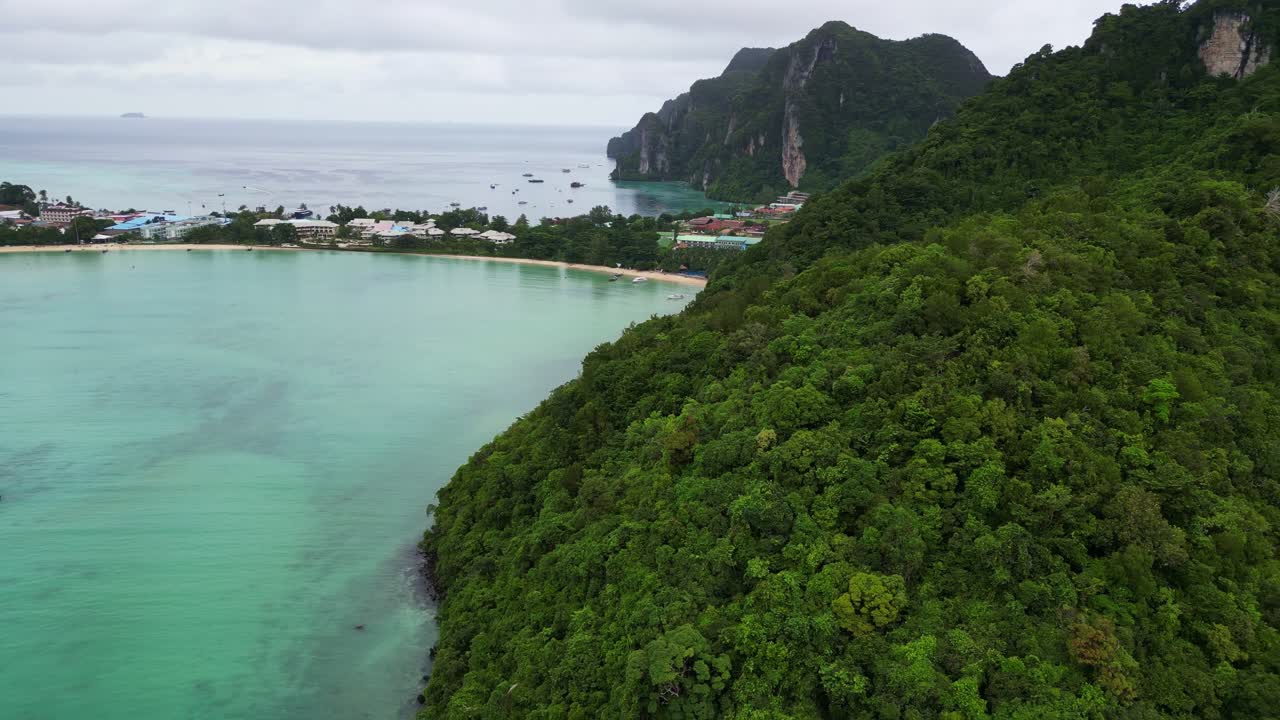 A lush green island surrounded by clear blue water, featuring rocky coastlines and sandy beaches under a cloudy sky.