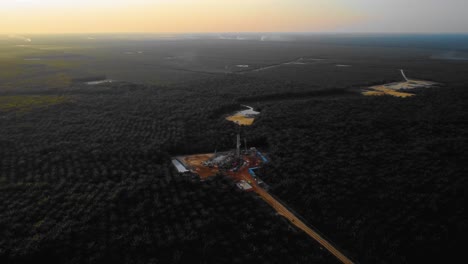imágenes cinematográficas de drones de 4k de la estructura del equipo de la plataforma de perforación en tierra para la exploración y explotación de petróleo en medio de la jungla rodeada de palmeras durante la puesta de sol y el alto precio del petróleo