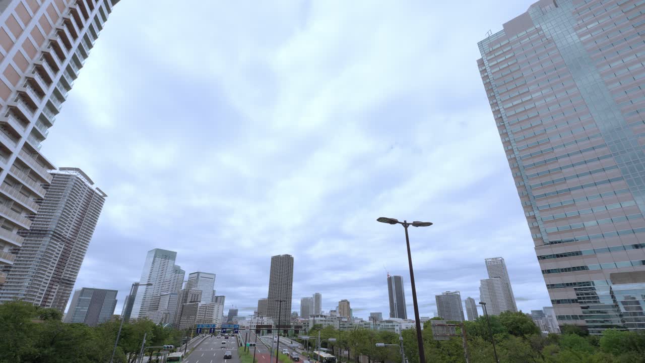 A low-angle shot of a Tokyo cityscape with a mix of tall modern skyscrapers and residential buildings against an overcast sky