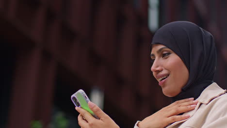 Close-Up-Of-Muslim-Businesswoman-Wearing-Hijab-Standing-Outside-Modern-Office-Getting-Good-News-About-Job-Offer-Or-Promotion-On-Mobile-Phone-1