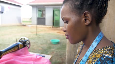 close up shot from the side of an african womans face as she sews clothing on a tailoring machine