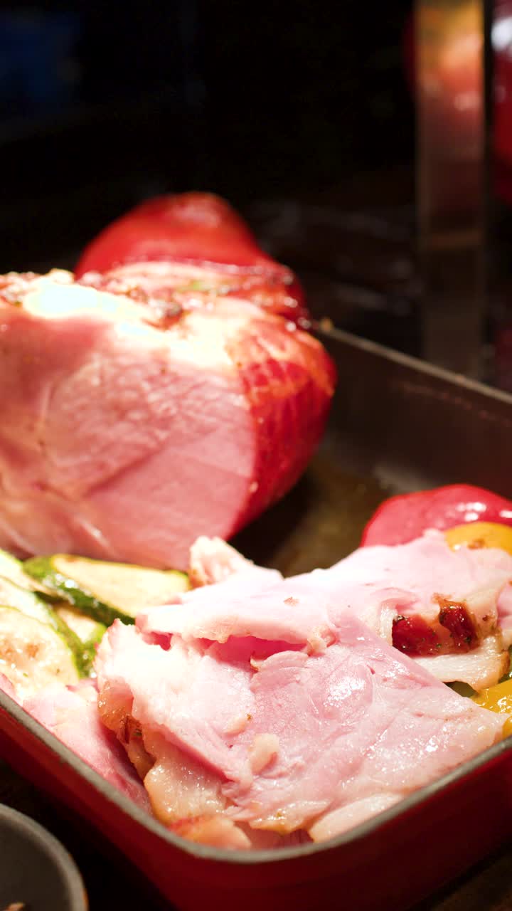 Primo piano di prosciutto arrosto affettato con verdure grigliate in una padella di ghisa rossa.