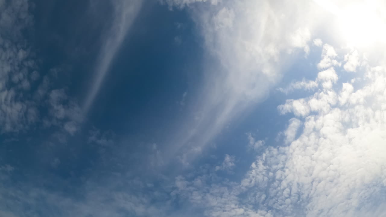 Spreading of light clouds by the blue sky. Sun is covered with soft cloudscape. Low angle perspective.