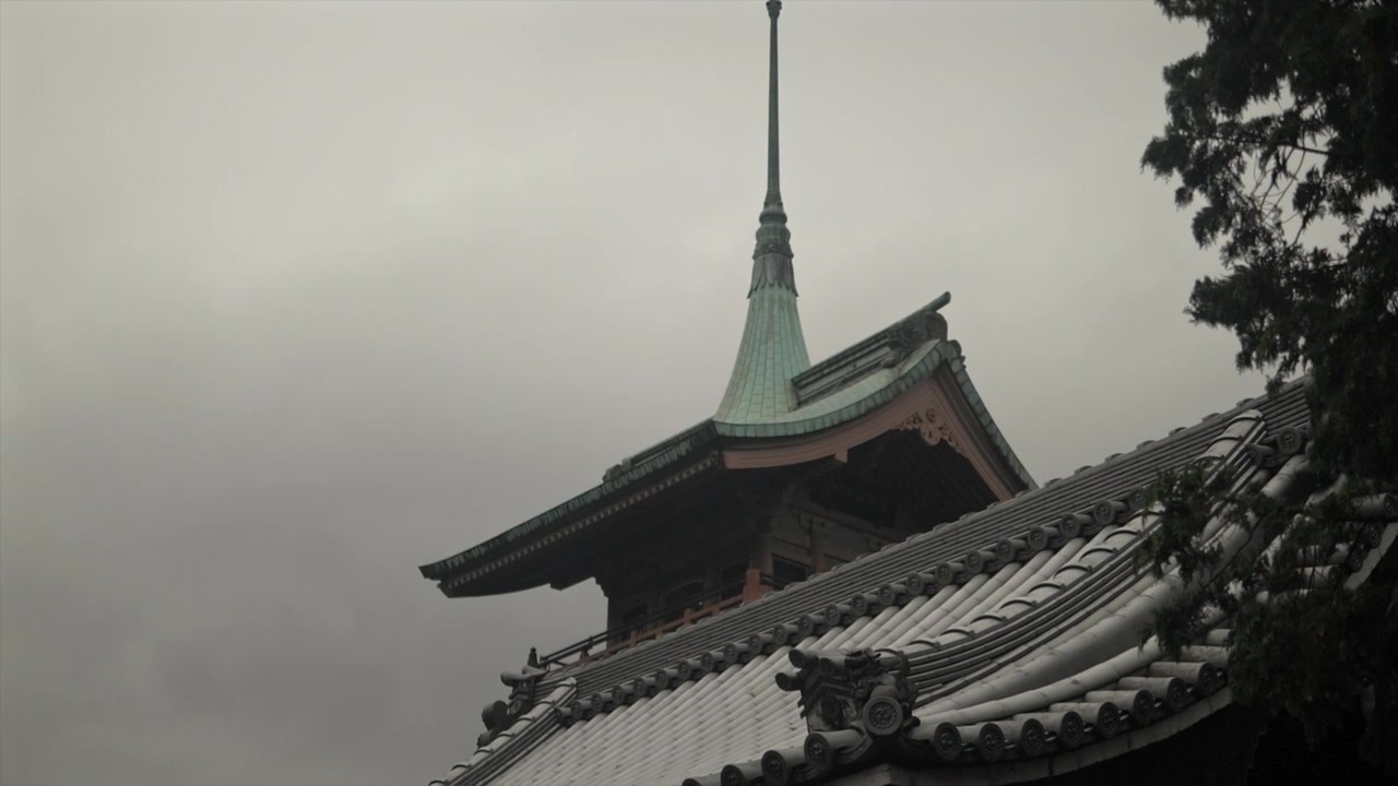 Traditionelt japansk tempeltag og spir under overskyet himmel i Kyoto, Japan